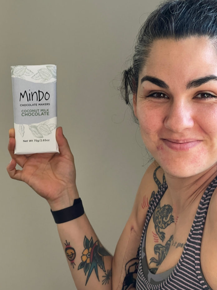 Tattooed woman with dark hair holding a wrapped chocolate bar