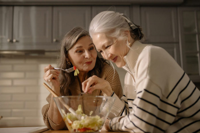 Women eating fruit salad in the kitchen.