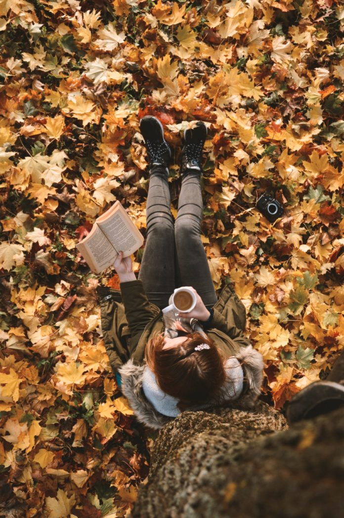 A woman sitting against a tree in the leaves.