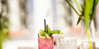 A short glass filled with a pink colored cannabis drink garnished with green leaves.