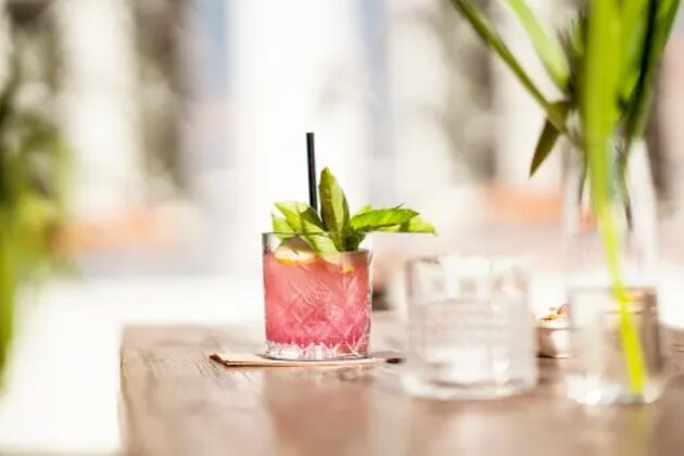 A short glass filled with a pink colored cannabis drink garnished with green leaves.