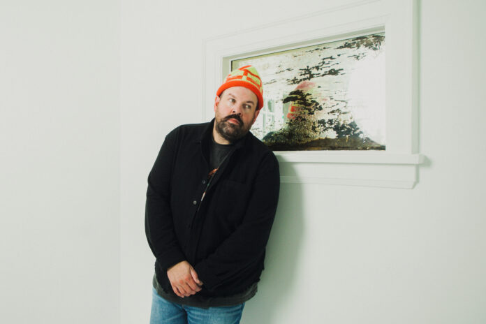 Man in orange hat in front of photo and white wall