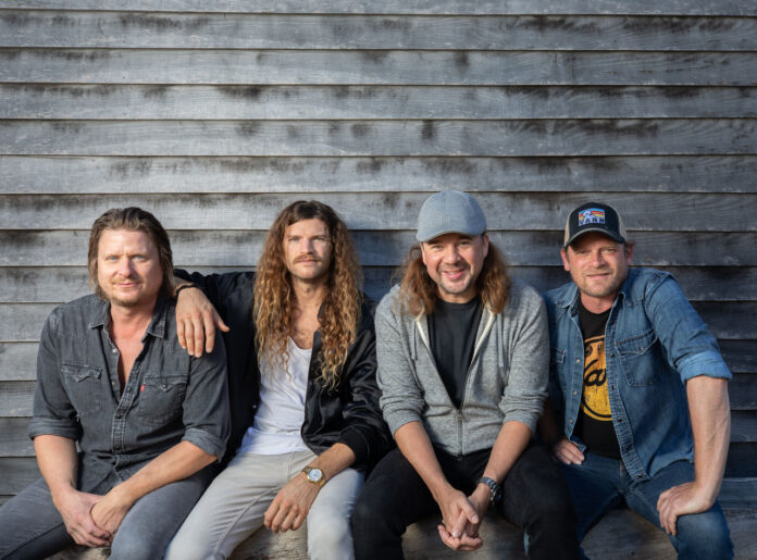 Four band members against rustic backdrop