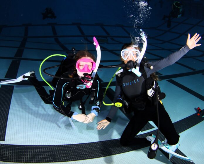Two kids scuba diving in pool.