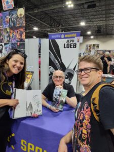Prolific writer Jeph Loeb (center) holds up a copy of “Batman: Hush,” which he wrote, and poses with fans Errin Stegich-Moloney (left), proudly holding up her signed copy, and Brian Maddaford (right). Photo courtesy of Errin Stegich-Moloney.