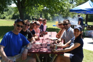 Company picnic with several people sitting around a picnic table.