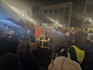 Jeff Kass in the middle of reading poetry, January 9. Ouyang is in the orange jacket, holding up one of the speakers for the people standing in the back. Photo by Drew Saunders.